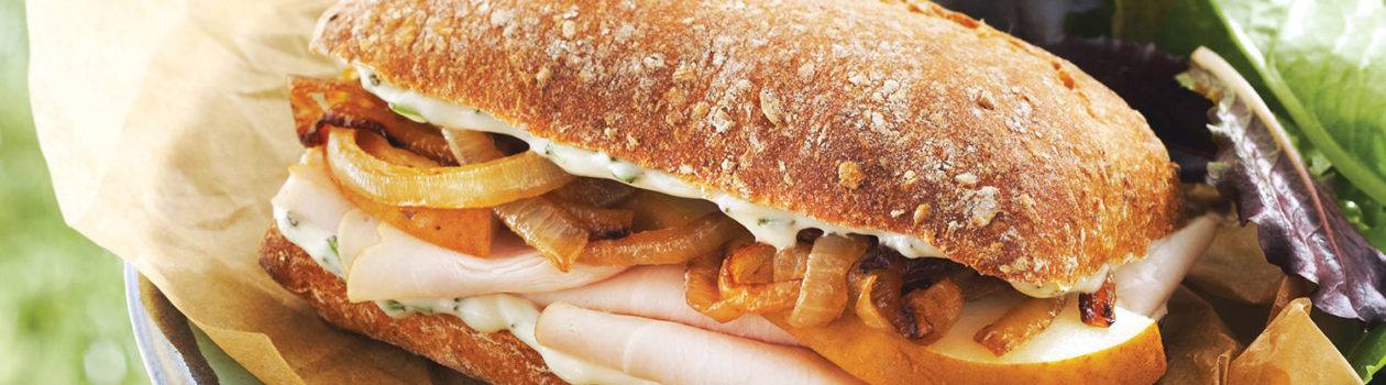 Ciabatta bun with sliced pork roast, caramelized onions and mayo, with a side of mixed greens