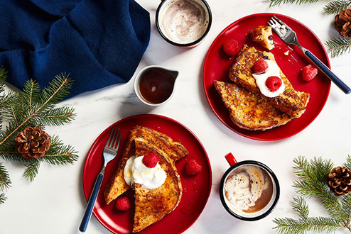 Egg nog french toast with cream and berries on round red plates.