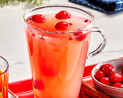 Tall clear heat-proof mug with tropical zero-proof cocktail, garnished with Cranberries