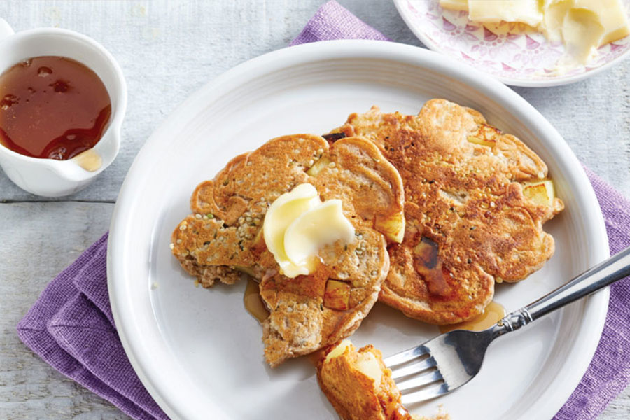 White plate with Apple & Hemp Seed Pancakes, cutlery and a side of syrup