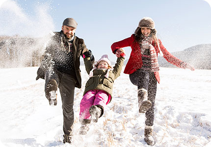 Family of three playing together in the snow on a suny day