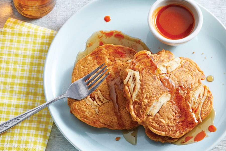 White plate with cutlery on side, filled with chicken pancakes and side of hot sauce