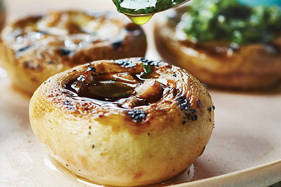 Close-up of mushroom caps filled with pesto sauce on a beige plate.