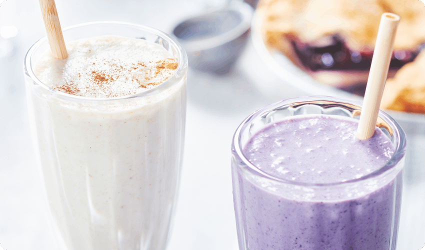 white marble surface with two milkshake glasses, one filled with a white milkshake, the other with a purple milkshake