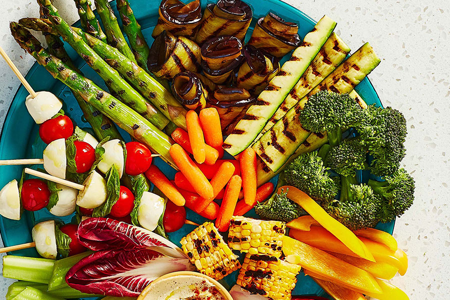 Zucchini sticks that have been grilled, piled on a plate with other bright vegetables.