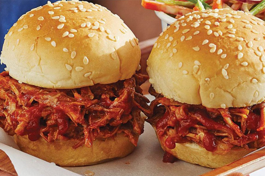 Side view of a hamburger bun piled with pulled pork and creamy coleslaw.