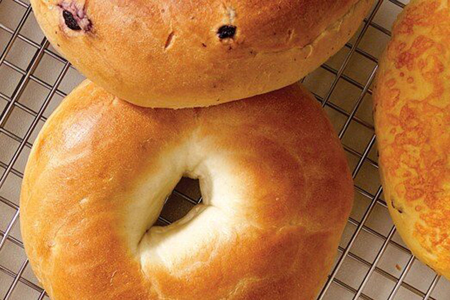 Various New Yorkâ€“style bagels on a wire rack over a white countertop.