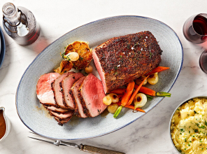 Sliced roast on a gray speckled tray served with roasted vegetables on a marble tabletop.