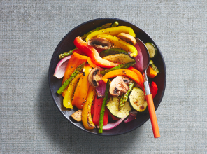 Deluxe mixed vegetable griller in a black bowl with an orange handled spoon.