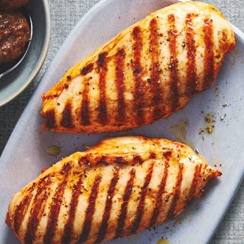 A light blue lavender plate topped with two grilled marinated chicken breasts. â€¯â€¯