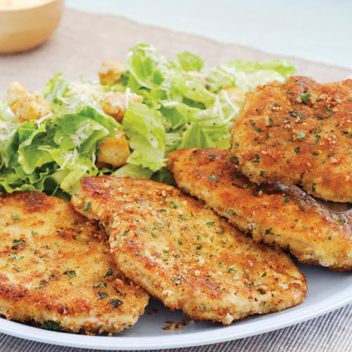 neutral tabletop with white serving platter with large portion of Caesar salad and four chicken schnitzels.