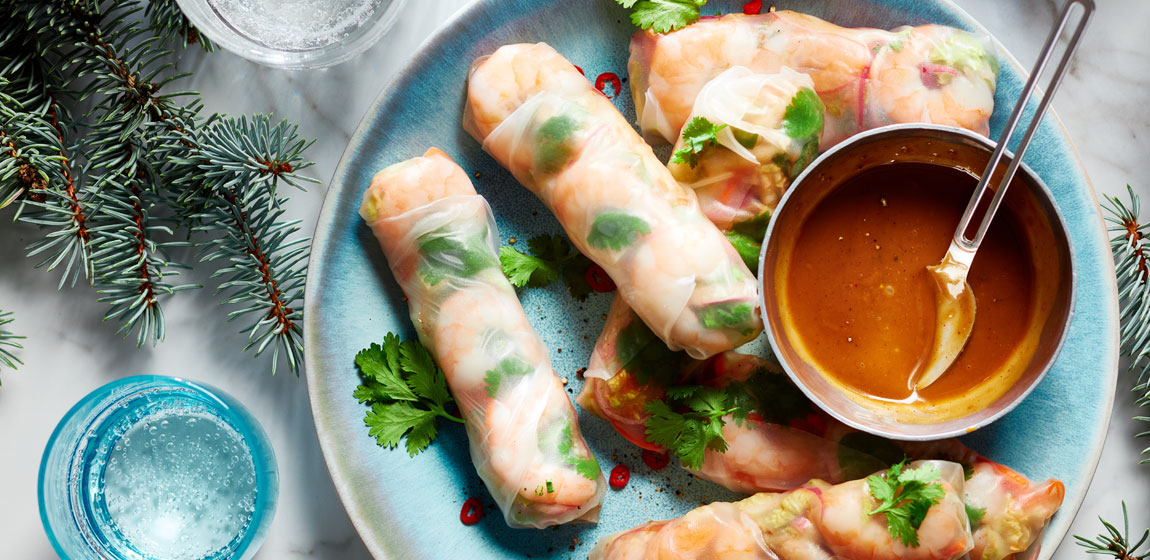 Round blue serving plate with fresh spring rolls in rice paper wrappers and a side of dipping sauce.