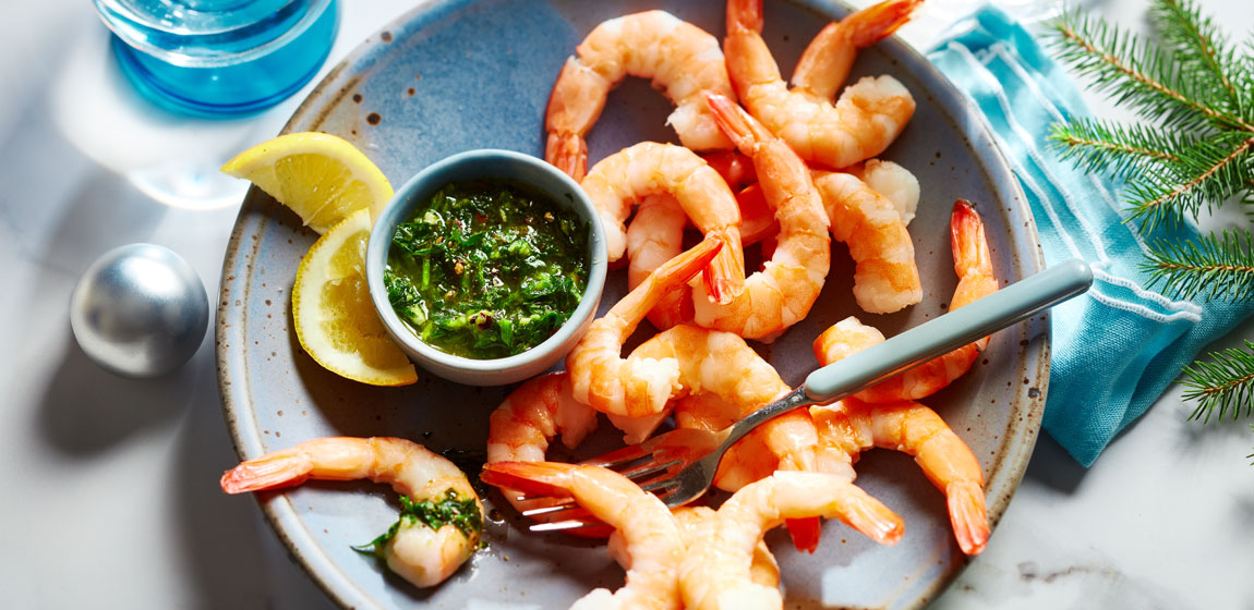 Blue serving plate with shrimps from a Compliments Naturally Simple Cooked Pacific White Shrimp shrimp ring, with a side of zhug dipping sauce.