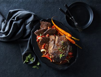 Cooked Sterling silver sirloin roast on a black serving platter garnished with carrots, red pepper slivers and gravy.