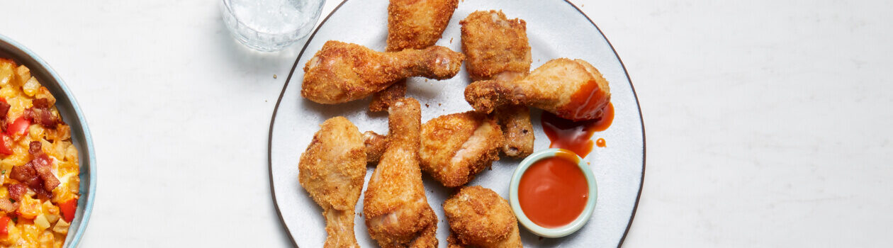 Light blue plate of chicken wing drumsticks with a side of hot sauce.