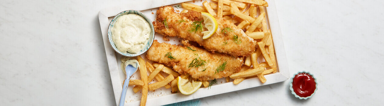 White rectangular plate full of fish and chips with a side of tartar sauce.