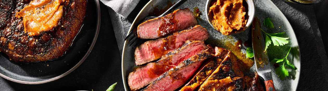 Grilled, sliced sirloin steak on a speckled gray platter with a side of the BBQ butter and a steak knife.