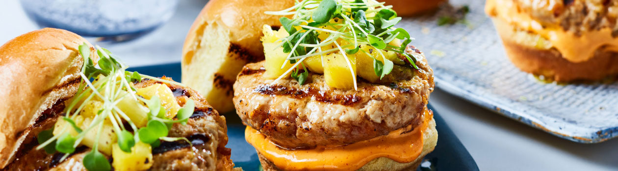 Korean-style pork sliders topped with pineapple cubes and micro greens on a blue plate.