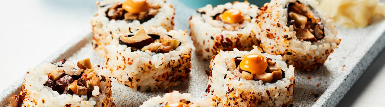 Several mushroom rolls sitting on a gray serving platter next to a little blue bowl of soy sauce.