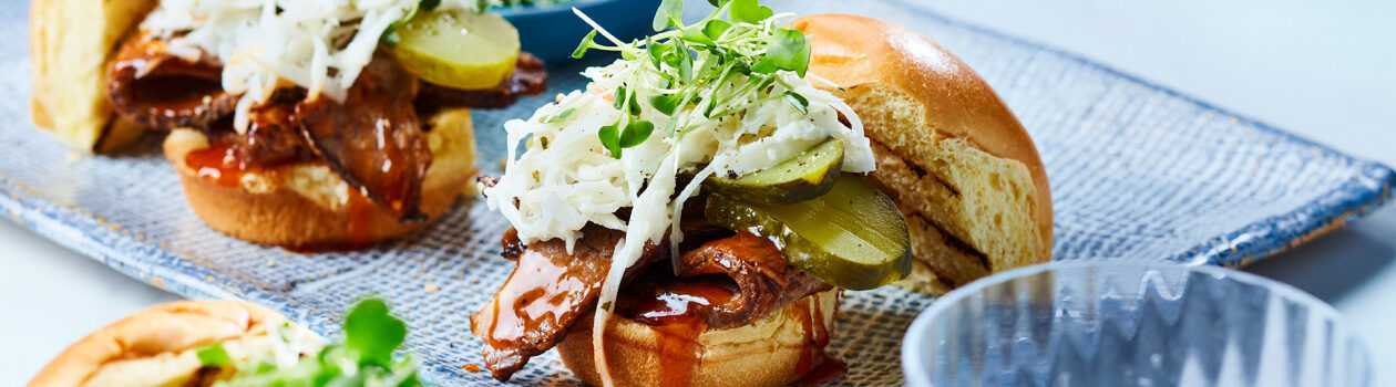 BBQ brisket sliders topped with creamy coleslaw and microgreens on a blue plate.