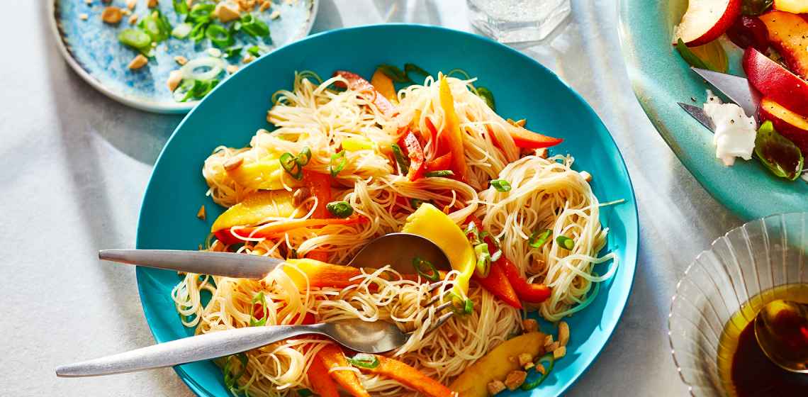 Blue plate topped with a Thai-inspired rice noodle salad sitting next to a plate