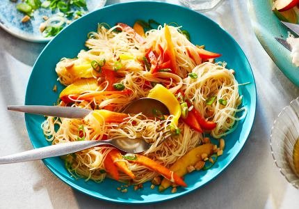 Blue plate topped with a Thai-inspired rice noodle salad sitting next to a plate