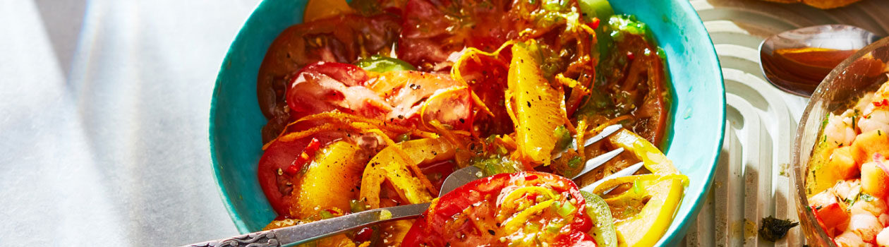 Heirloom tomato ceviche-style salad in a blue serving bowl with serving spoons.