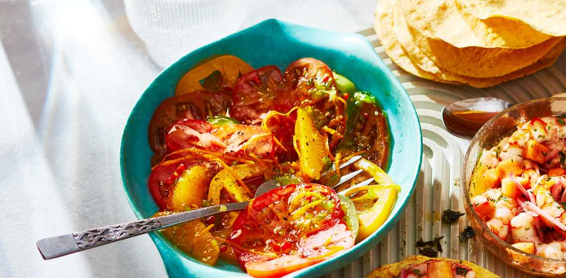 Blue bowl filled with Heirloom Tomato Ceviche-Style Salad with serving spoons.