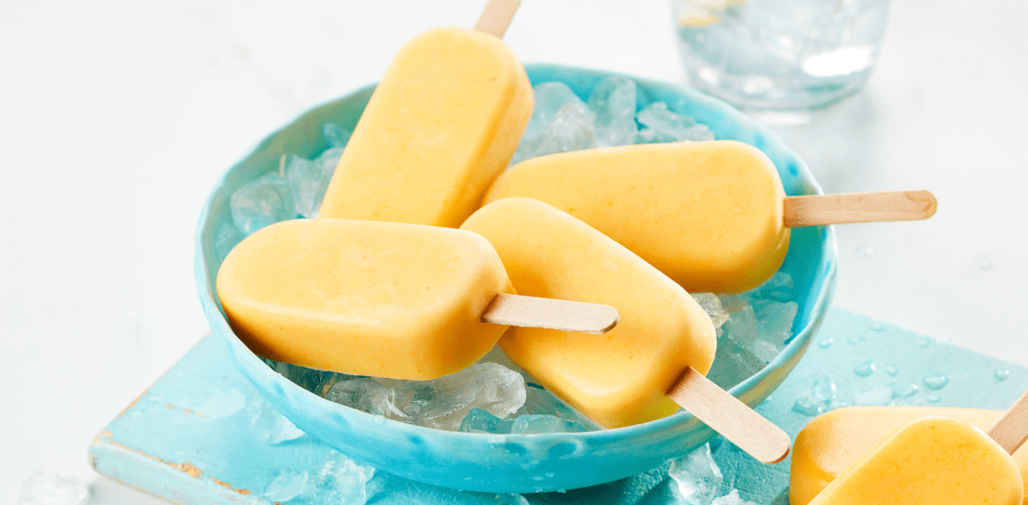 Several golden milk smoothie pops in a light blue bowl sitting a top ice.