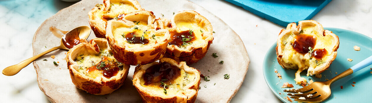 Mini French onion quiches made with hamburger buns on a beige plate next to a little bowl of chutney.