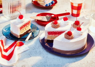 Triple-layer chocolate, vanilla and strawberry Neapolitan cake iced in pink with maraschino cherries, sitting atop a blue dessert plate with a fork next to it.