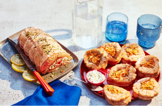 Sliced Mediterranean stuffed salmon on a red platter served with lime wedges next to a glass of water on a white marble tabletop.