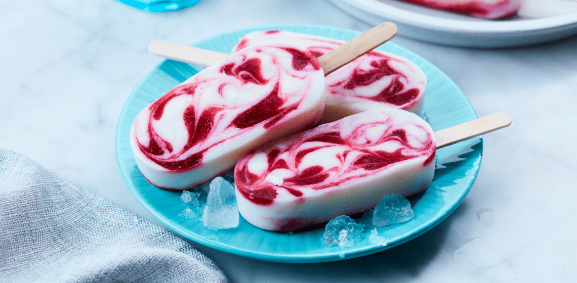 Swirled berry smoothie pops on a light blue plate with a few ice cubes around them.