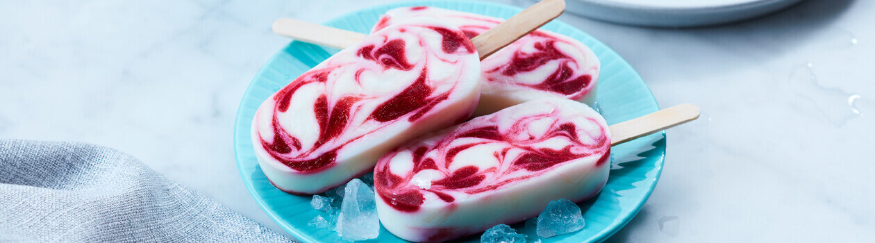 Swirled berry smoothie pops on a light blue plate with a few ice cubes around them.