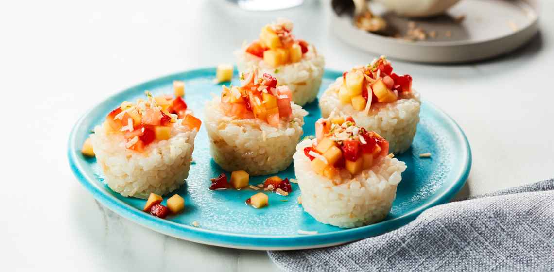 Fruit topped rice rolls like sushi, on a light blue plate.