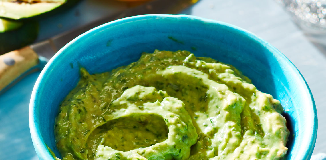 Blue bowl filled with a light green avocado tahini herb sauce.