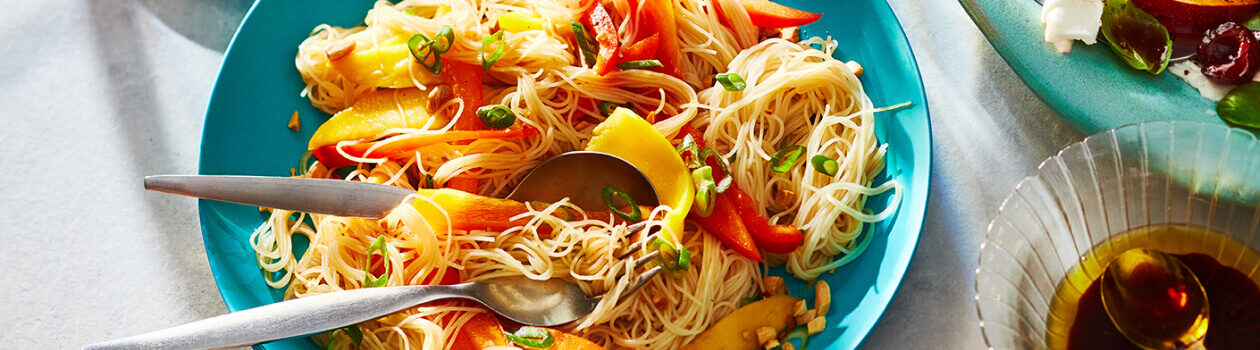 Blue serving platter with a Thai-inspired rice noodle salad on top with serving spoons.