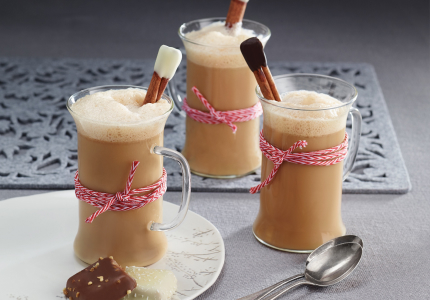 A grey table with three clear mugs of Gingerbread Almond Latte with cinnamon stir sticks and red and white twine wrapped around the middle.