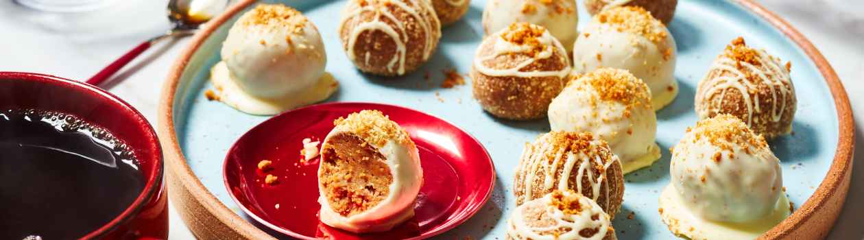 red serving platter of Biscoff Cheesecake truffles with one showing bite taken out, and a hot cup of tea off to the left of the platter.