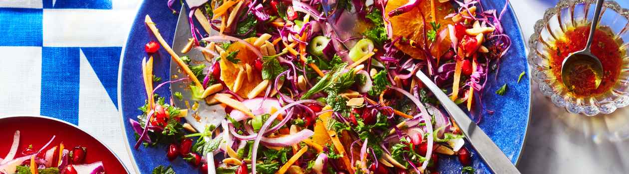 White marble surface with blue serving platter with tongs, cabbage and carrot Lebanese-inspired slaw, and red side plate filled with individual portion