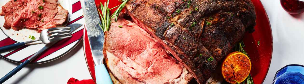 round red serving platter with moroccan-spiced roast beef, with slices cut on one end, and a roasted onion, rosemary and citrus garnish on the side