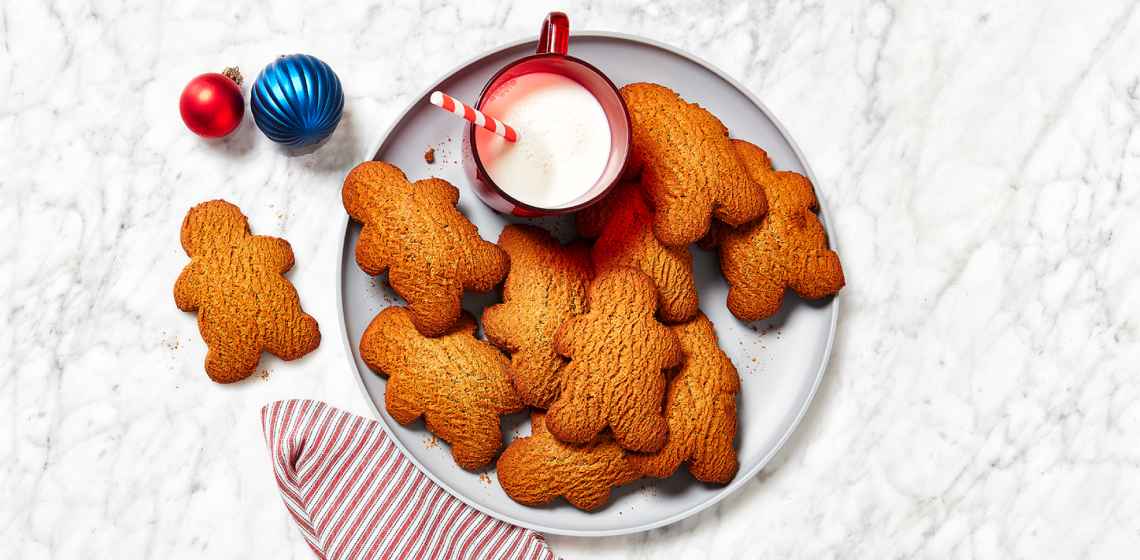 A round grey serving plate topped with gingerbread people, a red mug of milk, and a striped napkin.