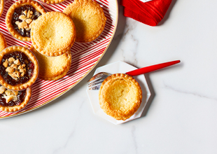 White side plate with almond tart on it next to large red and white striped platter of mixed holiday tarts