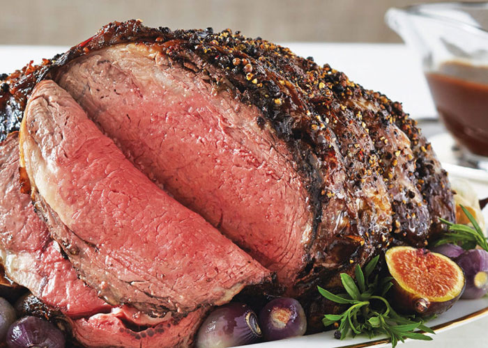 Sliced roast on white serving tray surrounded by figs, shallots, and rosemary