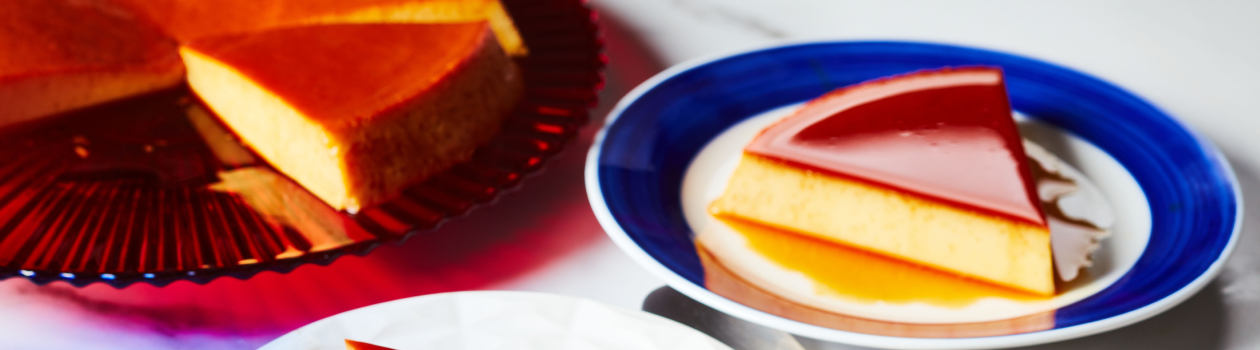 large red serving platter with caramel-topped round Mexican-style flan with two slices cut, one served out on blue-rimmed white side plate at right