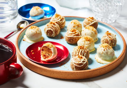 red serving platter of Biscoff Cheesecake truffles with one showing bite taken out, and a hot cup of tea off to the left of the platter.