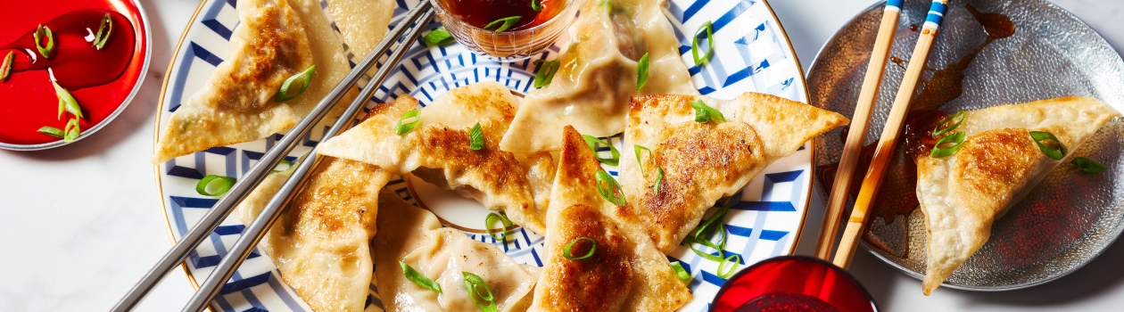 White and blue patterned plate with wonton wrapper pot stickers, green onion garnish, chopsticks and dipping sauce