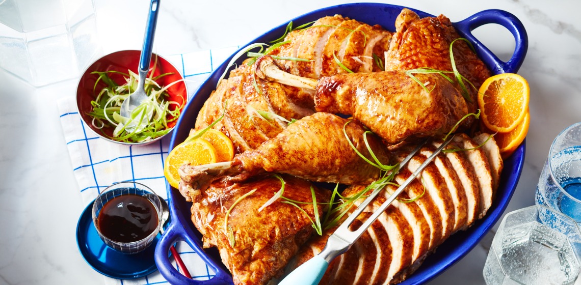 Blue serving platter with serving fork, sliced turkey breast and whole legs arranged with citrus slices and green onion garnish