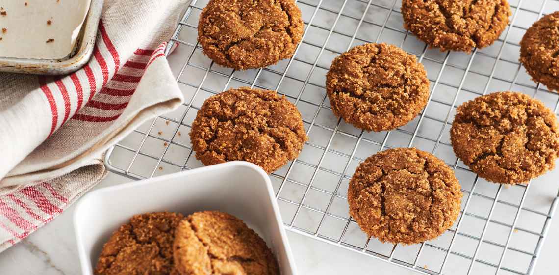 A marble counter with a cooling rack topped with crinkled ginger molasses cookies.