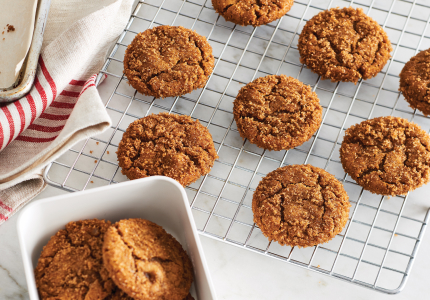 A marble counter with a cooling rack topped with crinkled ginger molasses cookies.